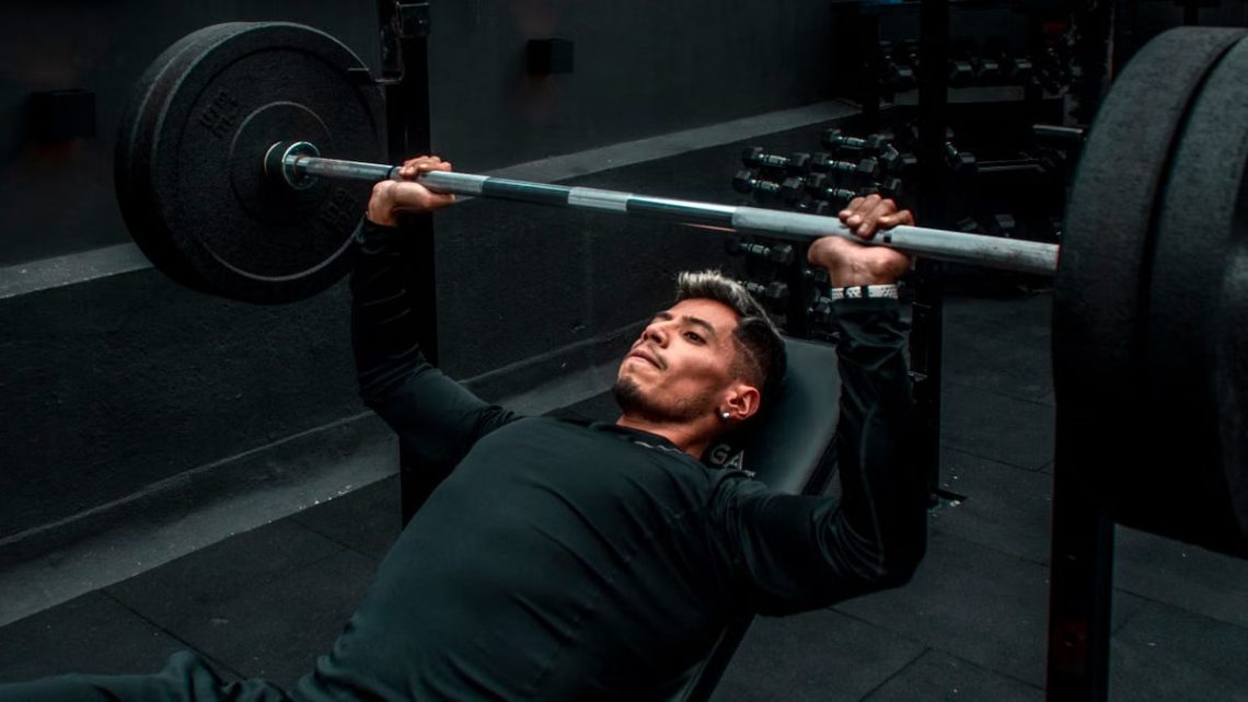Man performing bench press with heavy barbell in a gym setting, focusing on strength training.